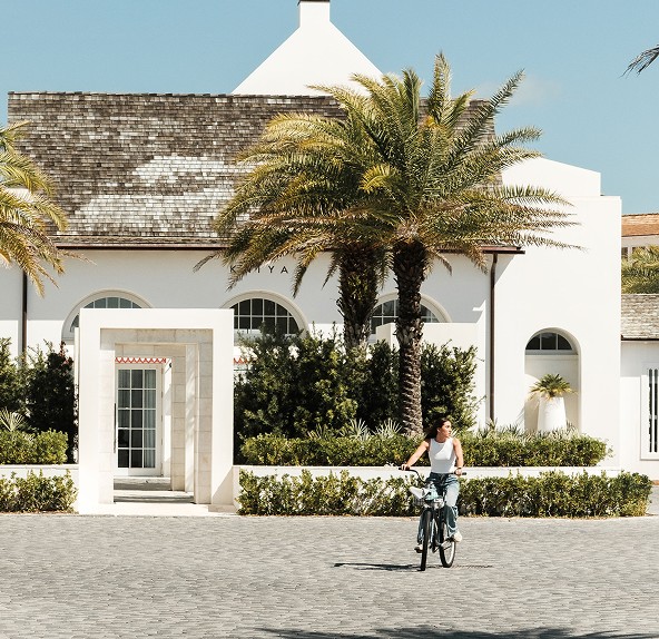 Cyclist riding past a white coastal building with palm trees on 30A